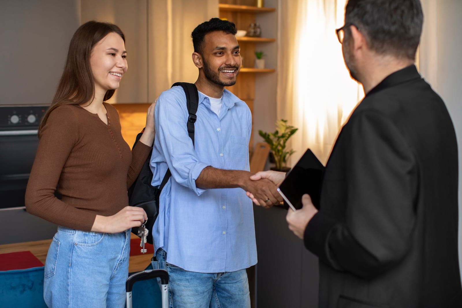 Un hôte accueille deux voyageurs souriants dans un appartement